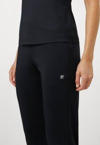 Sorte treningsebukser laget av elastisk stoff med slim fit, med en liten logodetalj på låret og glidelås-lommer.
