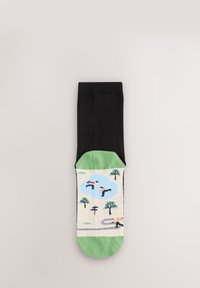 Chaussette noire montante avec un pied vert à motif représentant des arbres et des personnages sur un fond clair. Le matériau semble lisse avec des détails fins.