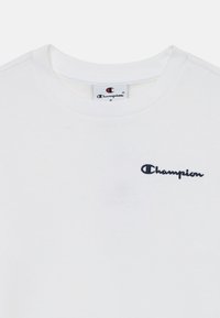 Vit bomulls-t-shirt med rund halsringning, prydd med en marinblå broderad "Champion"-logotyp på vänster bröst.
