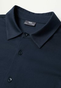 Polo bleu marine en tissu lisse, doté d'un col classique, de deux boutons, et d'une étiquette à l'intérieur du col.