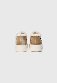 Pantofi din suede brown cu un brâu pufoș de crem, având o talpă groasă albă și un design cu spate rotunjit. Detalii cu texturi vizibile.