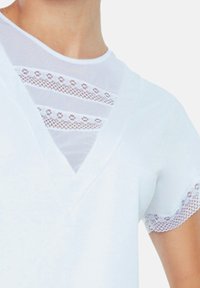 Biała bawełniana koszulka z dekoltem w serek, z przezroczystymi koronkowymi detalami na klatce piersiowej oraz koronkowymi obszyciami na krótkich rękawach. Gładka faktura.