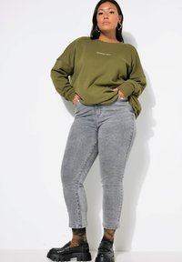 Sudadera de color verde oliva con el texto "WEEKEND VIBES", combinada con pantalones vaqueros ajustados grises y mocasines negros gruesos. Tela suave y corte relajado.