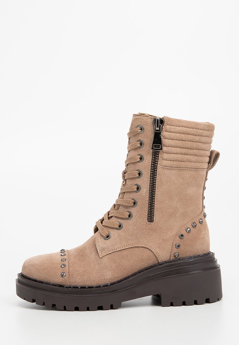 Botines de ante beige con punta redonda, cordones en la parte delantera, cremallera lateral y acentos de tachuelas plateadas en el talón. Suela de goma negra gruesa.