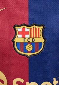 Grb FC Barcelone u obliku štita, s crvenim i plavim prugama, zlatnom loptom i vezom. Natpis glasi "FCB."