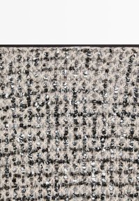 Tessuto beige decorato con paillettes nere e argentate, disposte in un motivo geometrico, creando una superficie testurizzata e riflettente.