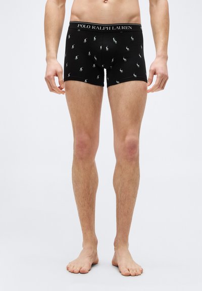 Μαύρα ανδρικά μπόξερ με λευκά λογότυπα Polo Ralph Lauren, που φορούνται από έναν όρθιο άνδρα μοντέλο, εμφανιζόμενο από τη μέση μέχρι τα πόδια επί απλού φόντου.