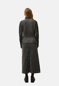 Czarny prążkowany sweter z golfem zestawiony z długą czarną spódnicą dżinsową. Teksturowany materiał, dopasowany w talii, z bocznym rozcięciem. Buty na grubej podeszwie.