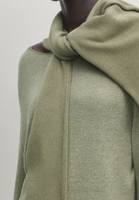 Light green knit sweater with an open neckline, featuring a matching scarf draped around the shoulders. Soft texture and relaxed design.
