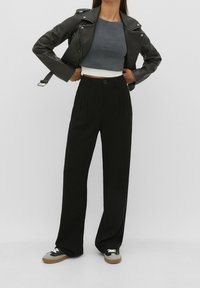 Czarne spodnie o szerokich nogawkach z przeszyciami z przodu, w połączeniu z szarym krótkim topem i czarną skórzaną kurtką motocyklową. Czarnoniebieskie i szare sneakersy dopełniają look.