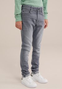 Světle šedé skinny džíny s pěti kapsami, s mírným vyblednutím, nošené s bílými teniskami a mentolovým dlouhým rukávem.