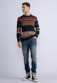 Gestreepte trui in marineblauw, rood, beige en grijs; gebreide textuur. Gecombineerd met vervaagde blauwe jeans en zwarte high-top sneakers.