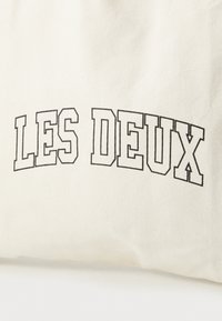 Off-white storpose med fet svart tekst "LES DEUX" i store bokstaver, buet design, med en glatt tekstur.