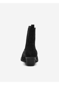 Bottine en daim noir avec un talon bas empilé, dotée d'une sangle de tirage et d'une couture décorative à l'arrière. Doublure intérieure lisse.
