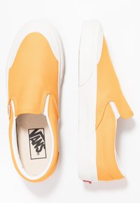 Orangefarbene Canvas-Slipper-Sneaker mit weißer Gummisohle und Akzenten. Verfügen über elastische Seitenteile und ein Logo auf der Innensohle. Strukturierte Oberfläche.