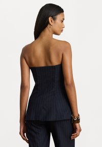 Uitgesneden strapless top in marineblauw streepjesstof. Gepaste pasvorm met gestructureerde buste en peplumdetails. Geen zichtbare hardware of versieringen.