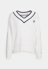 Hvid strikket sweater med V-hals, der har en ribbet krave i marineblå og hvid strib. Inkluderer et lille broderet logo på brystet.
