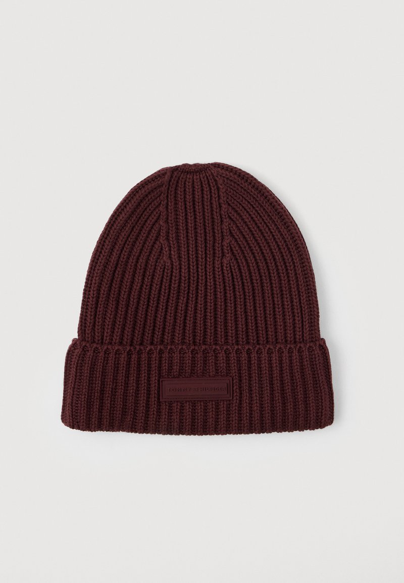 Ciemnobrązowa czapka beanie z prążkowanego materiału, z zagiętym mankietem i prostokątną metką marki z przodu na środku.