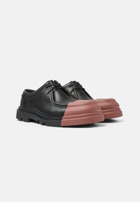 Chaussures en cuir noir avec un bout en caoutchouc rose arrondi, design à lacets, surface texturée et semelle noire épaisse avec un motif de sculpture.