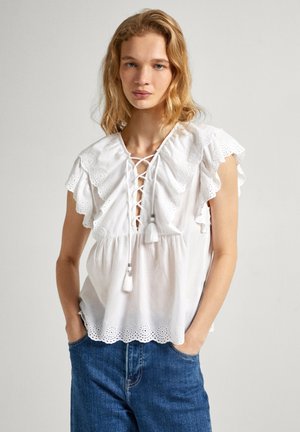 Blusa bianca in cotone con dettagli ad occhiello, maniche a volant, davanti con lacci e nappine decorative a contrasto sul colletto e sull'orlo.