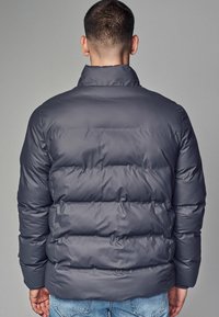 Sivá zateplená bunda s vysokým golierom, prešívaným dizajnom a elastickými manžetami. Hladký, lesklý povrch s horizontálnymi bafflemi.