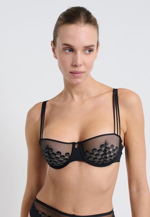 Soutien-gorge noir en maille transparente avec un motif brodé à bords festonnés, bretelles ajustables et design de sous-vêtements structuré.