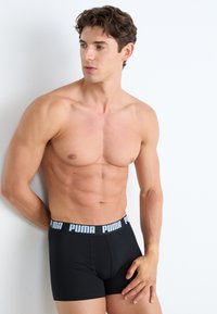 Boxeri negri din material elastic cu brâu cu marcă. Materialul pare neted, iar designul este ajustat. Modelul are o constituție musculară.