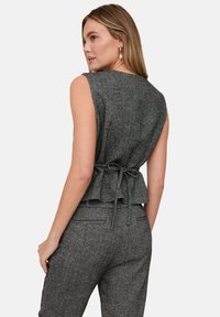 Graues ärmelloses Oberteil mit Fischgrätmuster, tailliertem Oberteil, gerafftem Saum und verstellbarer Schnürung hinten. Die Textur wirkt gewebt und weich.