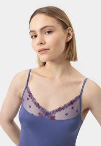 Blue sleeveless top with a sheer floral embroidered neckline featuring intricate patterns in red and blue. Smooth texture throughout.