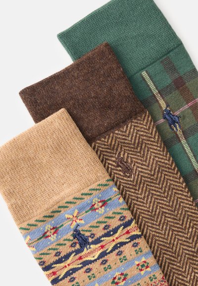 Trzy pary skarpetek: jedna beżowa z wzorzystym wzorem, jedna brązowa w jodełkę, a jedna zielona w kratę. Dzianinowy materiał o fakturze.
