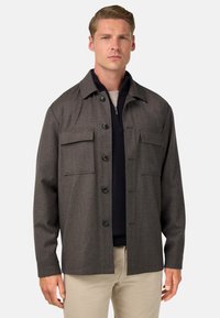 Chaqueta de franela gris con botones en el frente, dos bolsillos en el pecho y un dobladillo recto. Presenta un cuello con solapas y una tela texturizada.