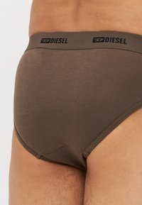 Brown cotton brief with a smooth texture, featuring a black branded waistband and snug fit, emphasizing a minimalist design.