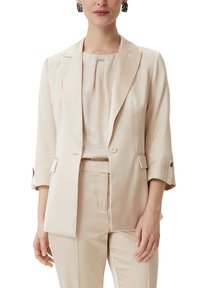 Beige blazer with notched lapels, front buttons, and rolled cuffs, paired with a matching top and tailored pants in a smooth fabric.