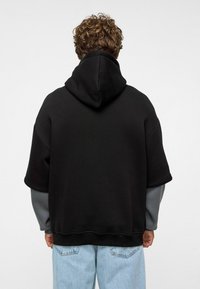 Zwarte oversized hoodie met een capuchon, voorzien van korte mouwen en een contrasterende grijze binnenlaag. Gecombineerd met lichtblauwe denim jeans.