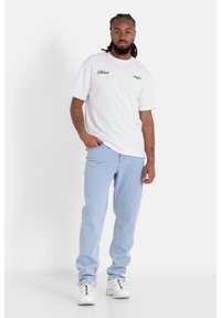 Camiseta blanca de manga corta con acentos impresos, combinada con vaqueros de color azul claro y zapatillas blancas, con un ajuste relajado y una textura suave.