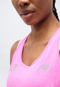 Κοντινό πλάνο ενός ατόμου που φοράει ροζ αμάνικη αθλητική μπλούζα New Balance με ορατά λογότυπα στο στήθος.