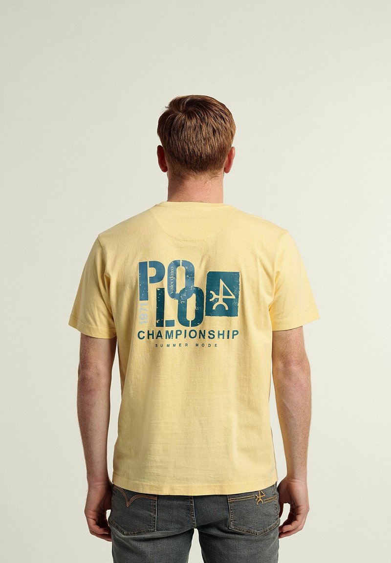 Camiseta de algodón amarilla con un gráfico azul que dice "Campeonato Polo" y un logo en la parte trasera. Mangas cortas y cuello redondo.