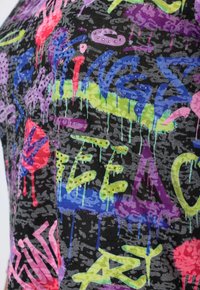 Schwarzer Stoff mit bunt graffitiartigen Texten in Pink, Blau, Grün und Lila, verziert mit Strassakzenten und einem strukturierten Hintergrund.