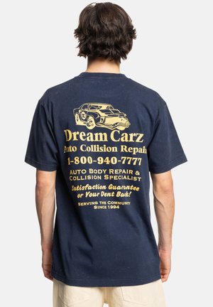 Marineblauwe t-shirt met een gele grafische afbeelding op de achterkant, inclusief een illustratie van een vintage auto en tekst voor een schadeherstelservice.