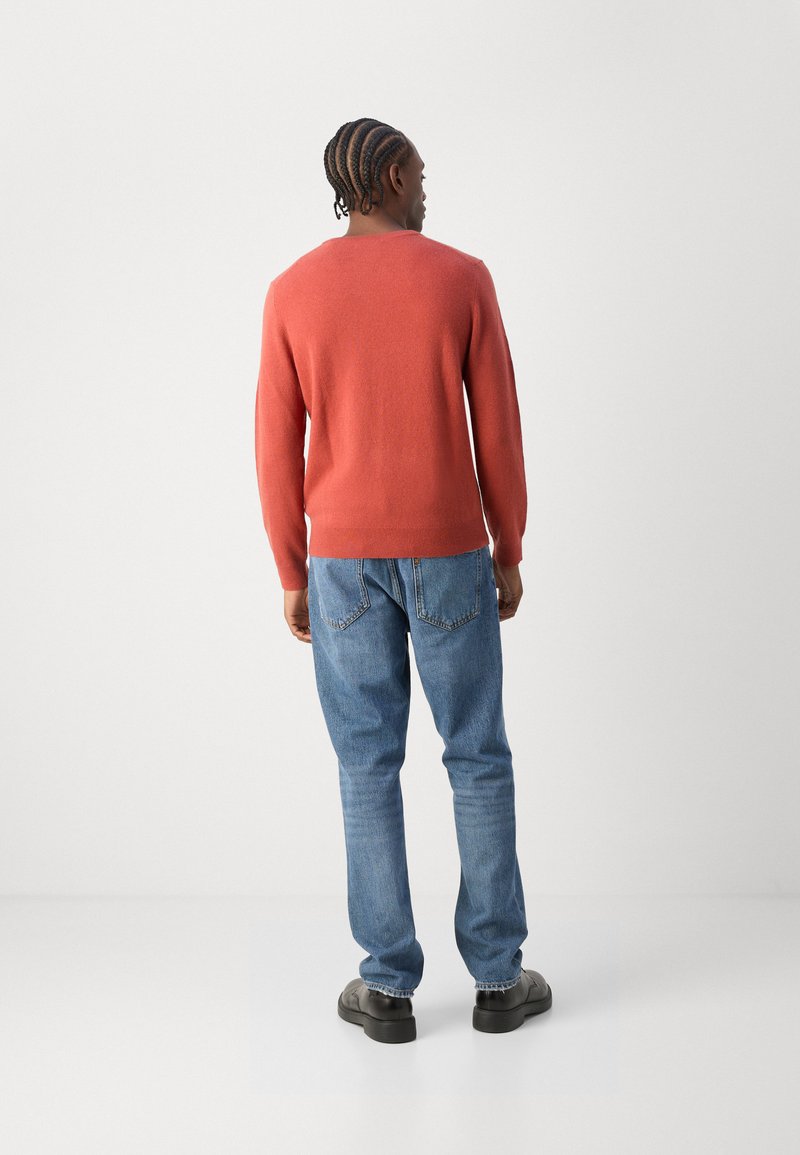 Rot gestrickter Pullover mit langen Ärmeln, Rundhalsausschnitt und geripptem Saum, kombiniert mit blauen Jeans und schwarzen Schuhen, von hinten gezeigt.