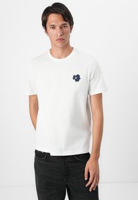 White cotton t-shirt with a crew neck and short sleeves, featuring a navy blue floral design on the left chest. Smooth texture, classic fit.