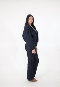 Granatowa krótka kurtka z dużymi klapami i bufkami na rękawach, zestawiona z ciemnymi, rozszerzanymi spodniami dżinsowymi oraz beżowymi butami na obcasie.