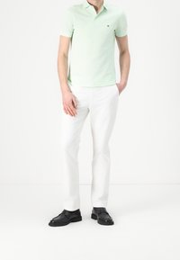 Jasnozielona koszulka polo z kołnierzykiem, zestawiona z białymi spodniami i czarnymi mokasynami. Szczegóły obejmują małe logo na koszulce.