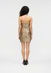 Φόρεμα χωρίς τιράντες με χρυσές παγιέτες, εφαρμοστή γραμμή, μήκος πάνω από το γόνατο και κάθετο ριγέ μοτίβο, συνδυασμένο με μαύρα ψηλοτάκουνα παπούτσια.