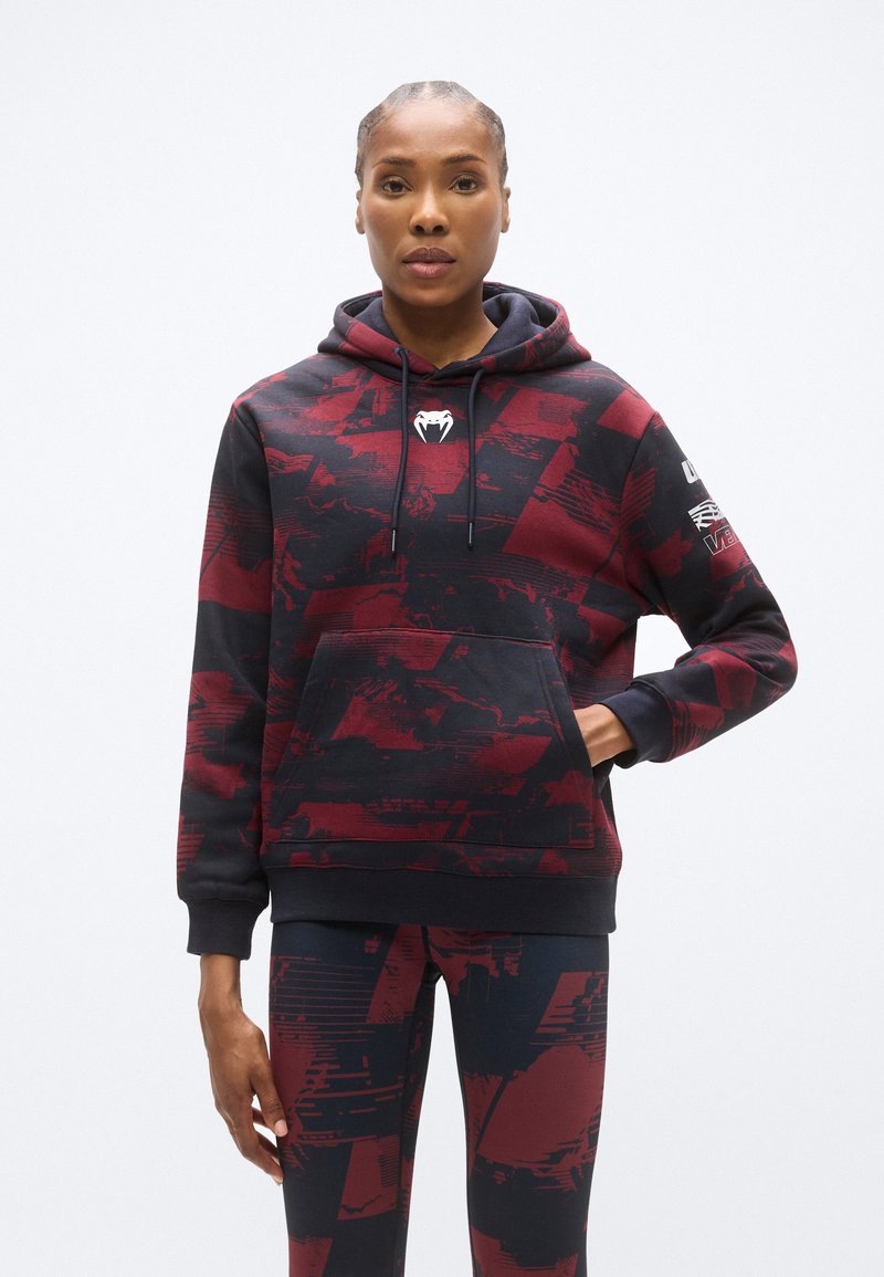 Sweat à capuche bleu marine foncé avec un motif abstrait rouge, doté d'une poche kangourou à l'avant et d'un logo sur la poitrine et la manche.