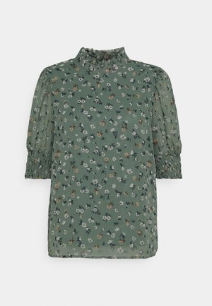 Grüne Blumenbluse mit hohem, gerafftem Kragen, aufgepufften Ellbogenlangen Ärmeln und gesmokten Manschetten.