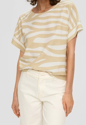 Woman wearing beige and white zebra-striped short-sleeve blouse tucked into high-waisted off-white pants against a plain background.
