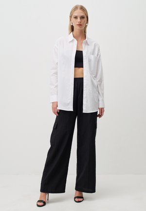 Witte button-up shirt over een zwart crop top, gecombineerd met wijde zwarte cargobroek. Het shirt heeft een borstzak en opgerolde mouwen.