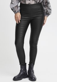 Svarta byxor i konstläder med en slät textur, slim fit design och hög midja. Matchas med svarta ankelstövlar med remmar.