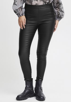 Czarne spodnie z sztucznej skóry o gładkiej fakturze, slim fit, z wysokim stanem. W zestawieniu z czarnymi botkami do kostek z paskami.